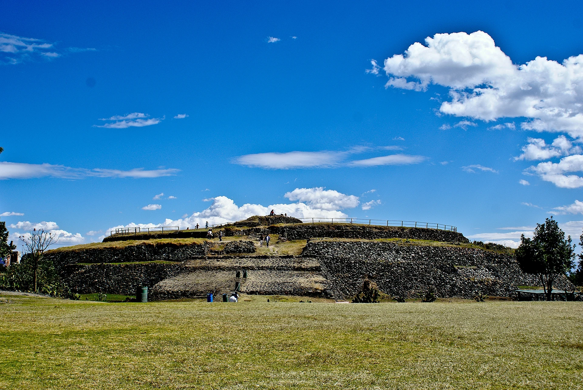 La pirámide circular y escalonada de Cuicuilco bajo un cielo azul, con pasto al frente, Ciudad de México