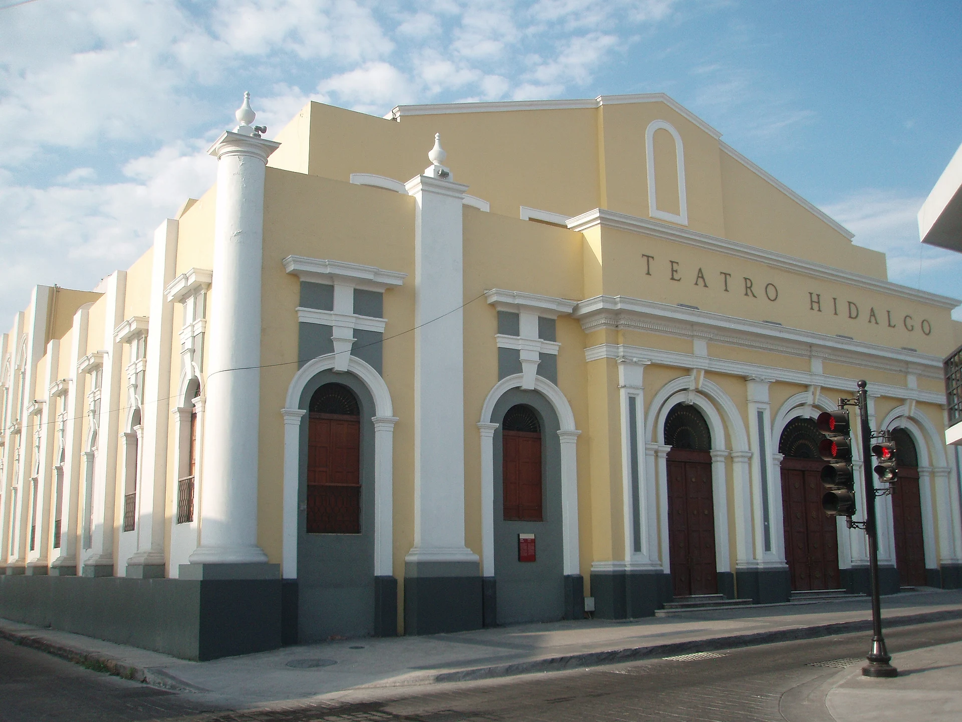 The pale yellow Teatro Hidalgo in downtown Colima, with white columns, arched doorways and its name across the facade