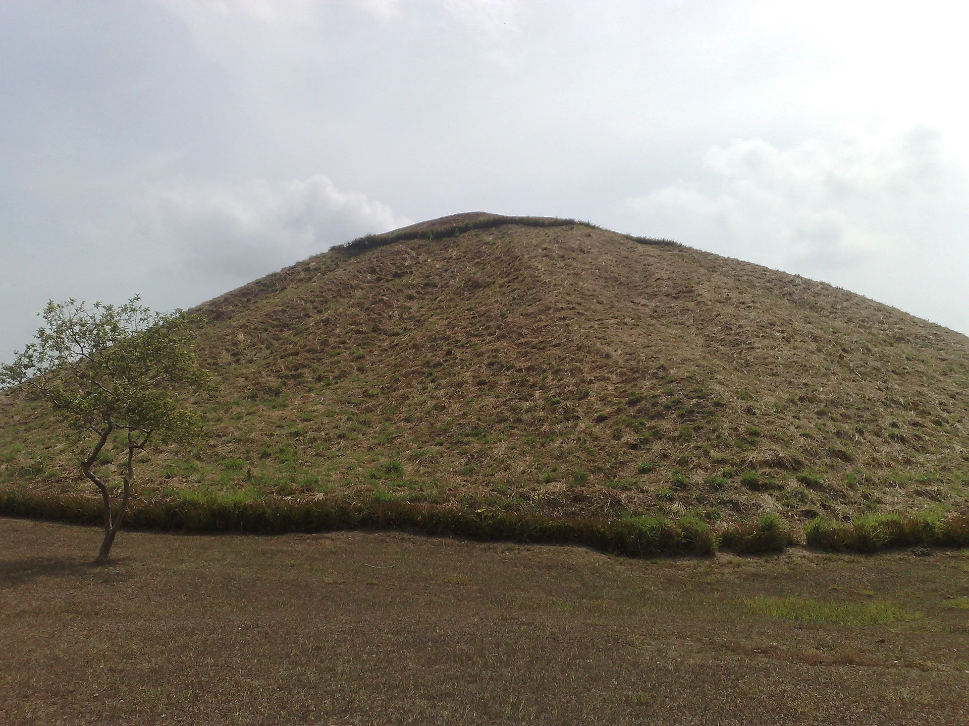 The south face of La Venta's Great Pyramid, a grass-covered clay mound under a cloudy sky, Tabasco