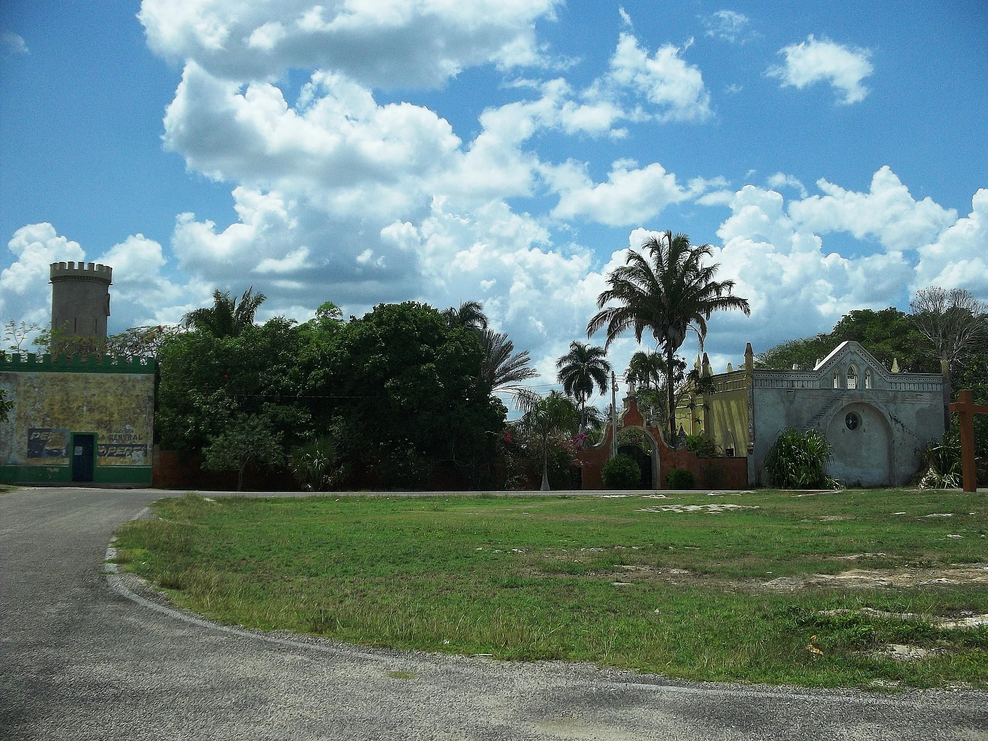 A tower of the Chenché de las Torres hacienda rising behind trees and a lawn by the road, Yucatán