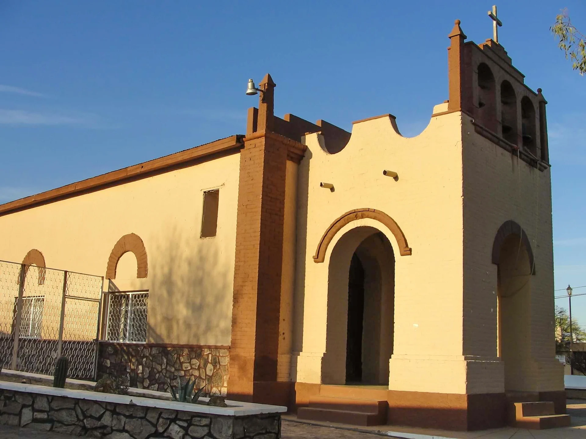 Templo de San Francisco de Asís en Átil, Sonora, pintado de crema y ladrillo, con remate ondulado, puerta en arco y campanario, bajo un cielo despejado