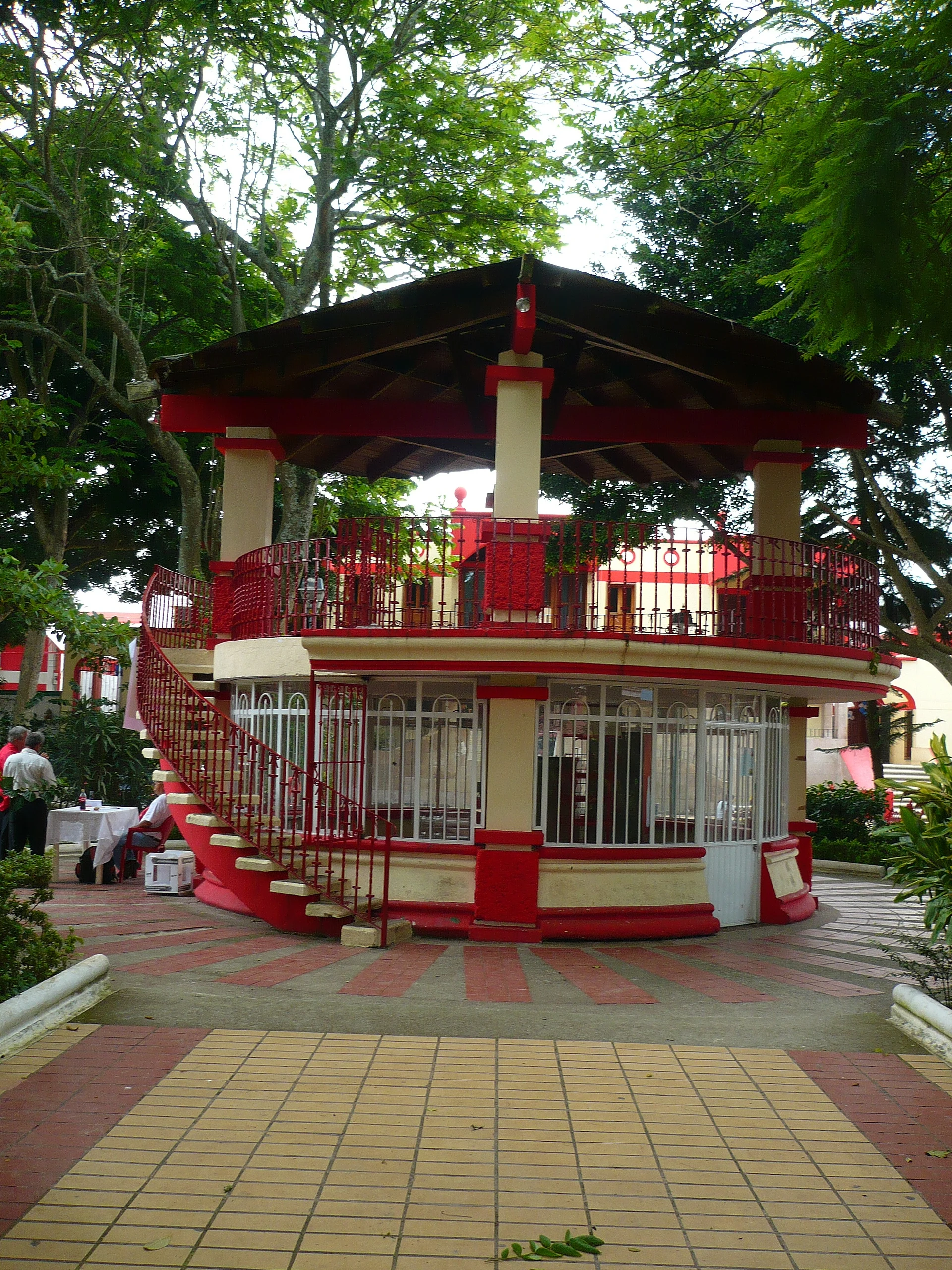 Two-storey red and cream kiosk under shade trees in the main square of Alto Lucero, Veracruz