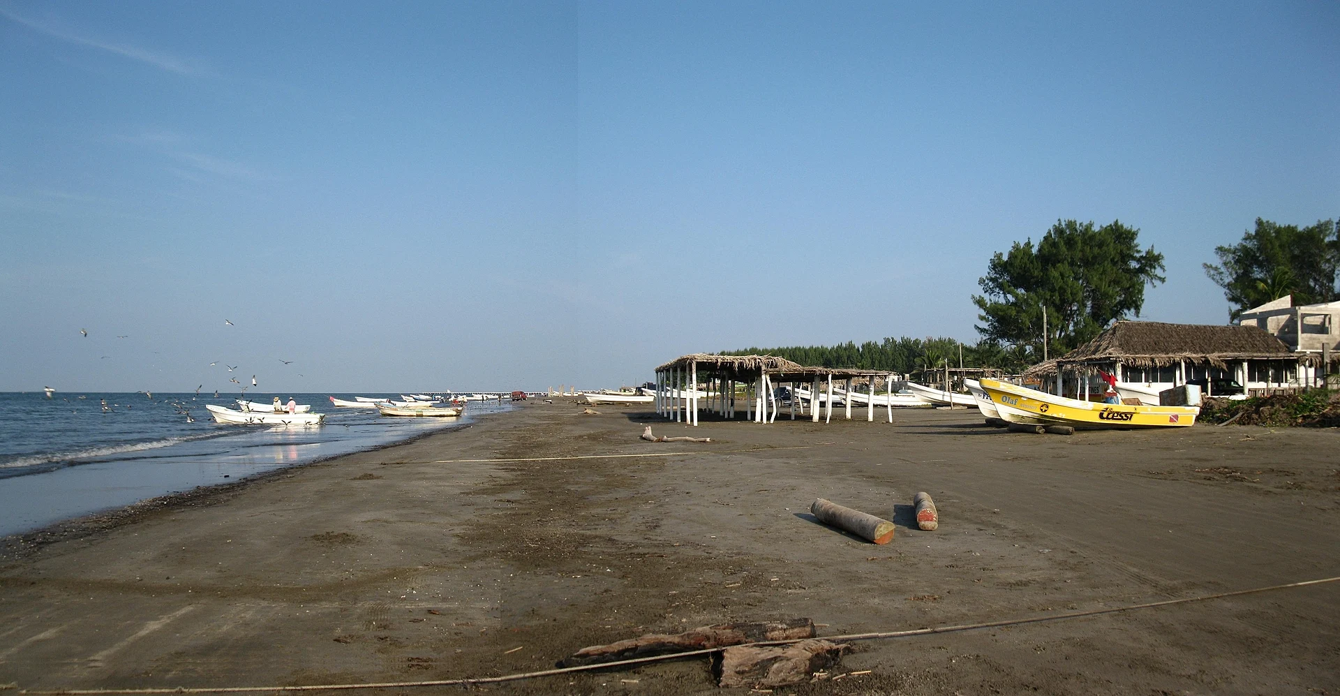 The dark-sand beach at Antón Lizardo with fishing boats pulled up by palm-thatched palapas, Veracruz