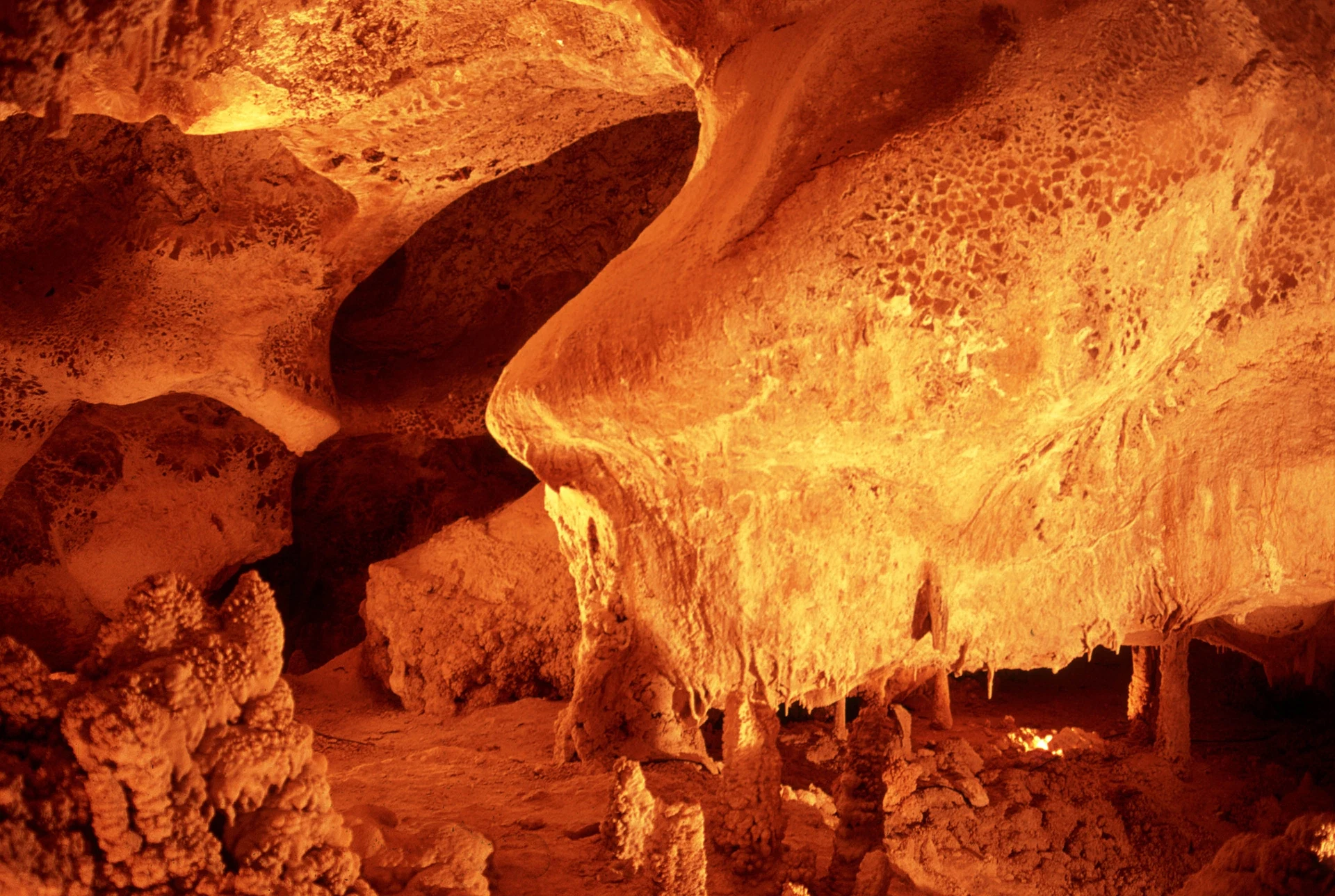 Formaciones de caliza y estalactitas iluminadas en tonos naranjas dentro de las Grutas de Coyame, Chihuahua