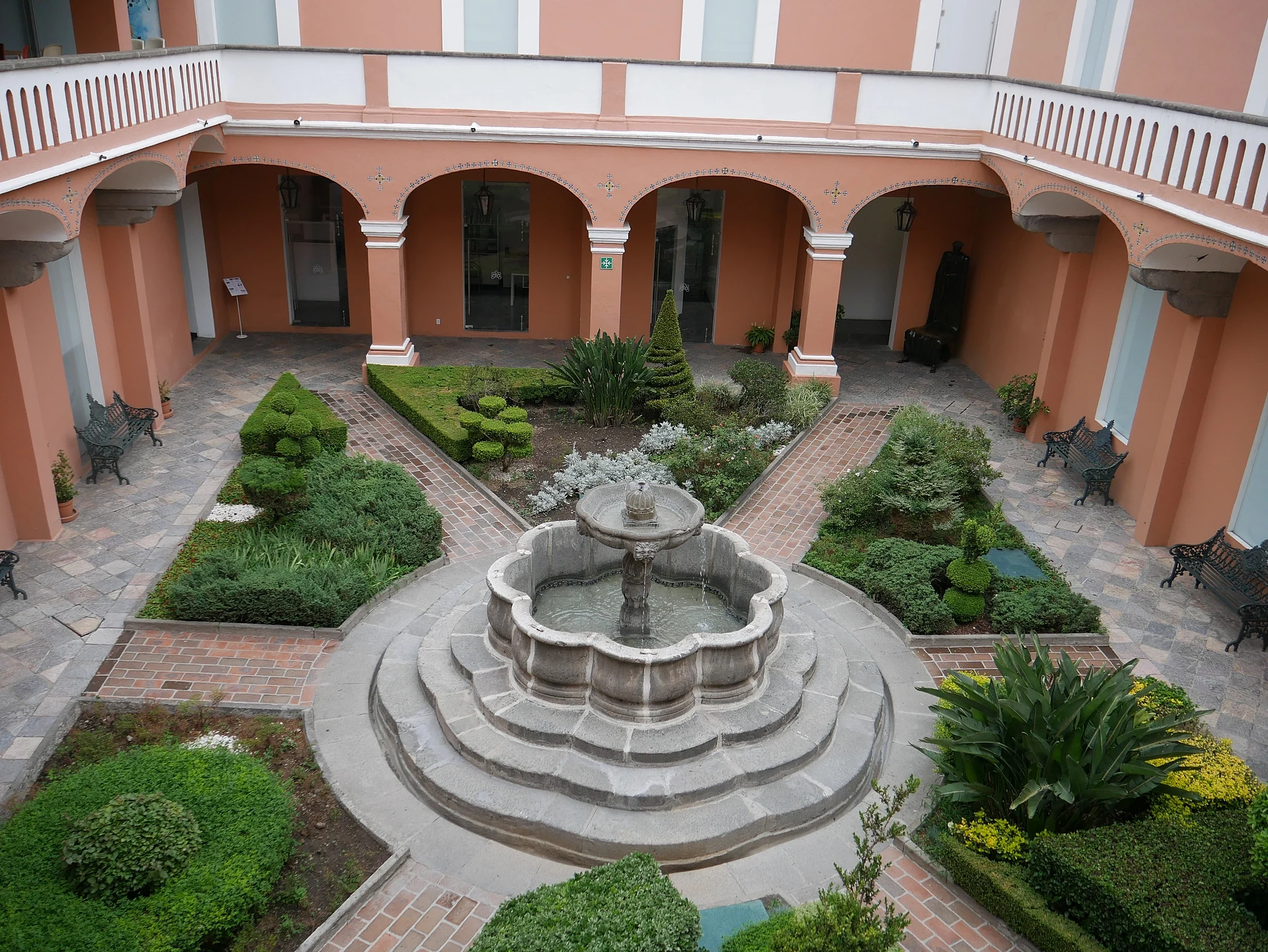 Arcaded colonial courtyard of the Museo Amparo with a stone fountain and garden beds, seen from the upper floor, Puebla