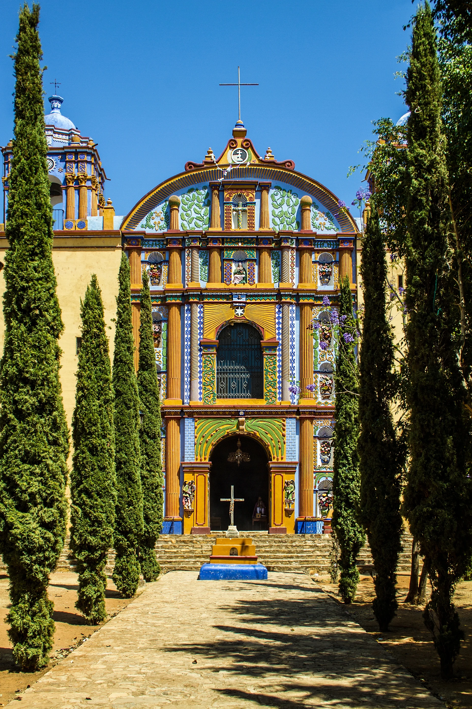Iglesia pintada de Santa Ana Zegache, con su fachada de colores y el camino flanqueado de cipreses, Oaxaca