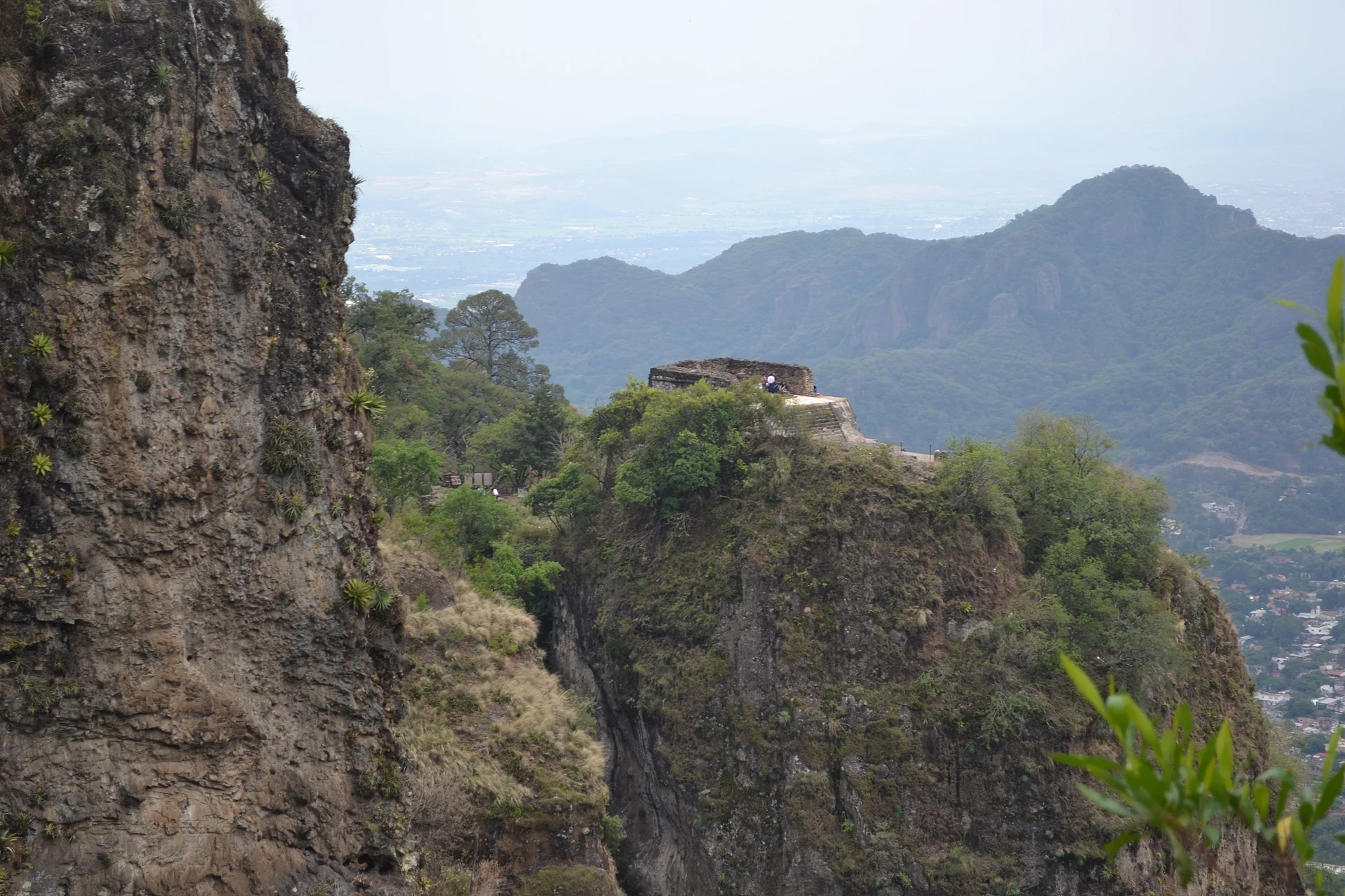Cliffs of the Tepozteco ridge with the pyramid on a forested outcrop and the sierra beyond, Parque Nacional El Tepozteco, Morelos
