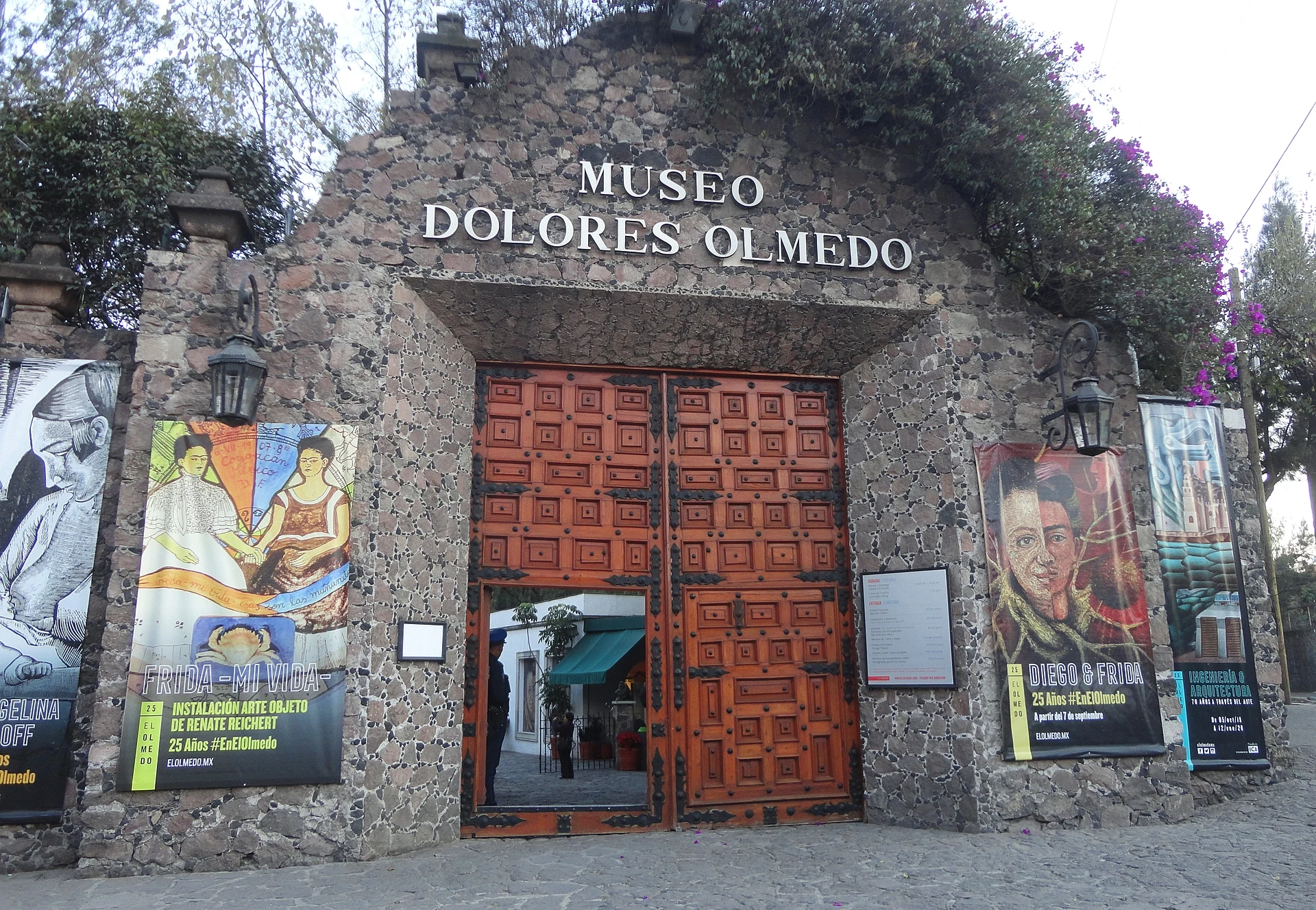 La portada de piedra del Museo Dolores Olmedo en Xochimilco, con puertas de madera labrada y mamparas de exposiciones, Ciudad de México