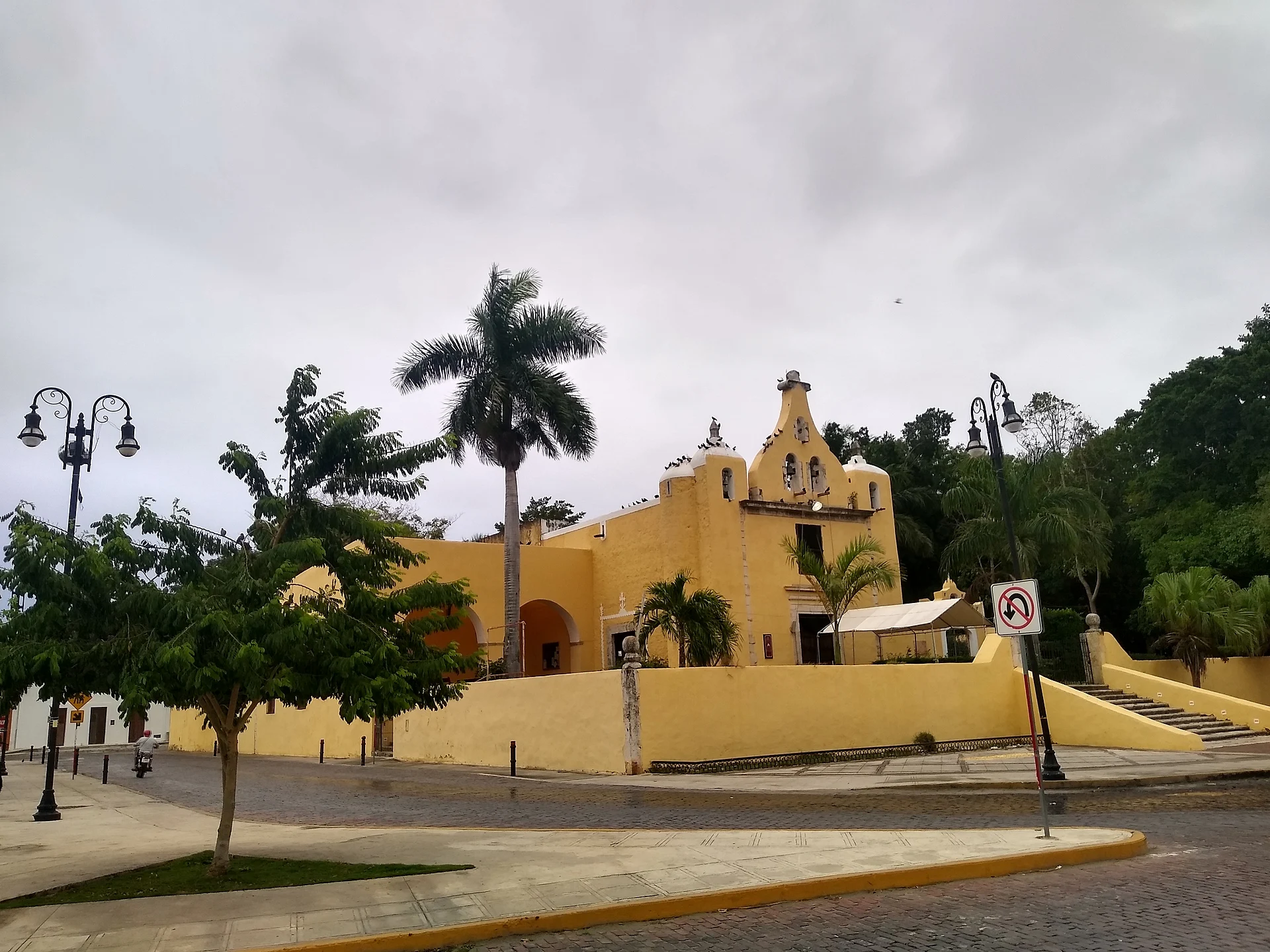El parque de La Ermita con palmeras y faroles, y detrás la capilla amarilla de Santa Isabel, Yucatán