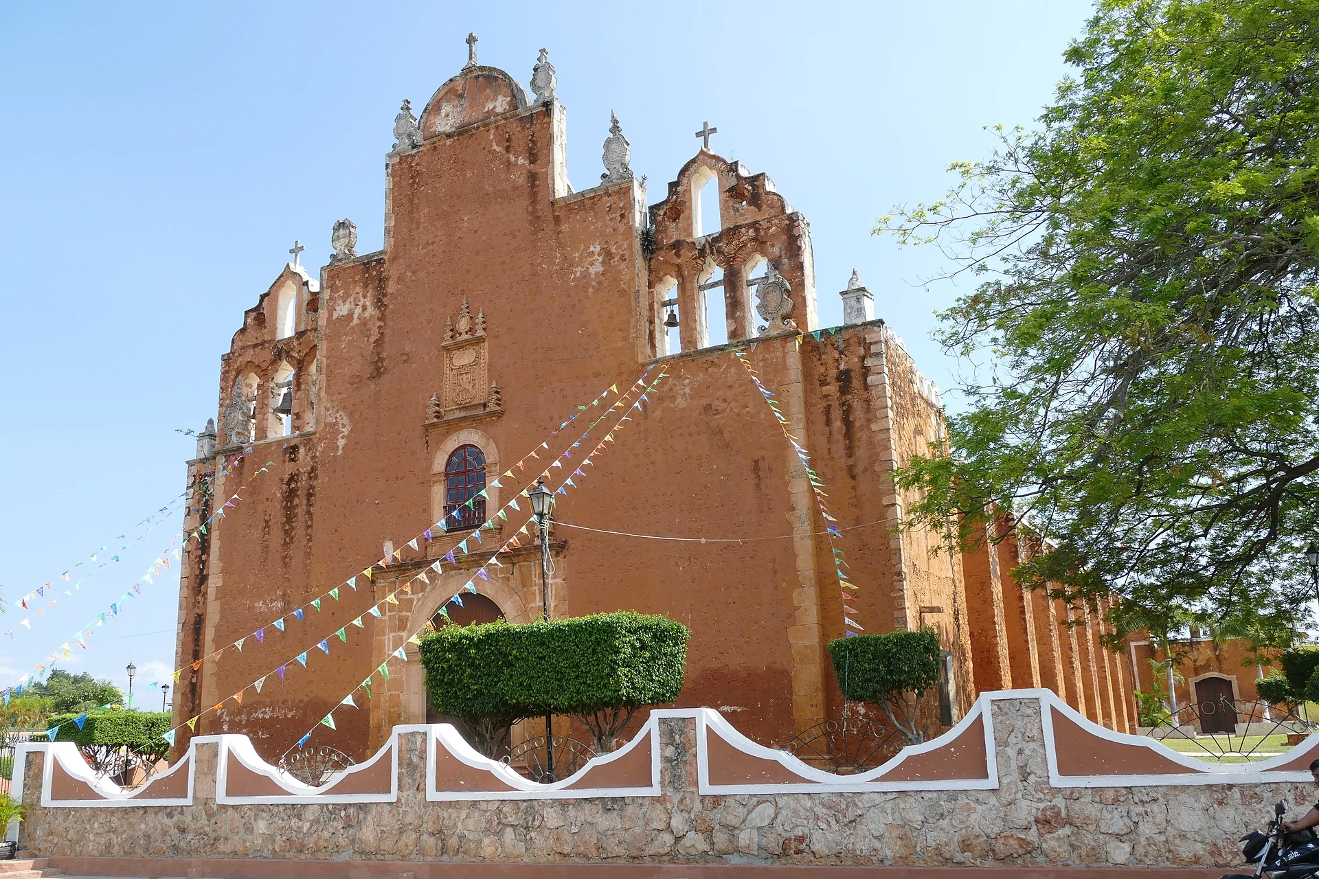 Weathered stone facade of the church of San Juan Bautista under papel picado, Tekax, Yucatán