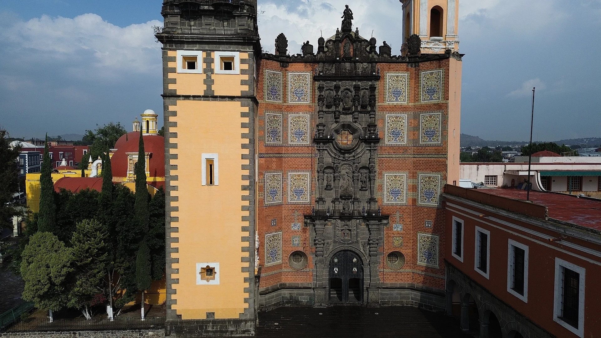 Brick and tile facade of the San Francisco convent church in Puebla, with its carved stone portal and yellow bell tower, San Francisco "El Origen"