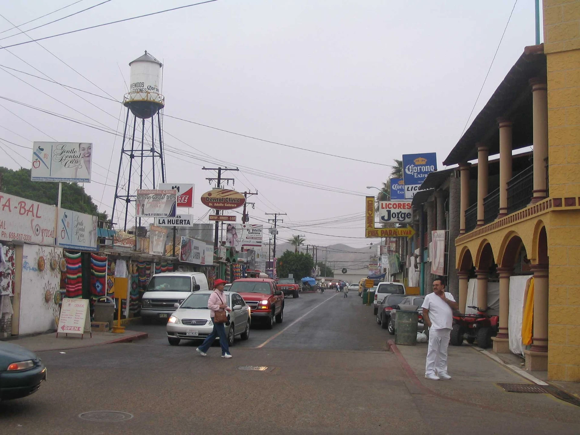 La Calle Dos de Los Algodones, con letreros de clínicas dentales, puestos de artesanía y portales, y la torre de agua del pueblo al fondo, Baja California